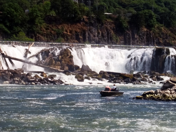 People fish from a small boat in front of a large waterfall