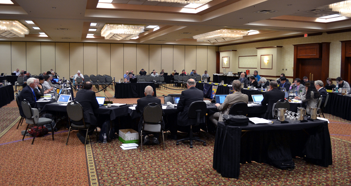 At a Council meeting, a group of people in professional dress sit around a u-shaped table in a hotel ballroom