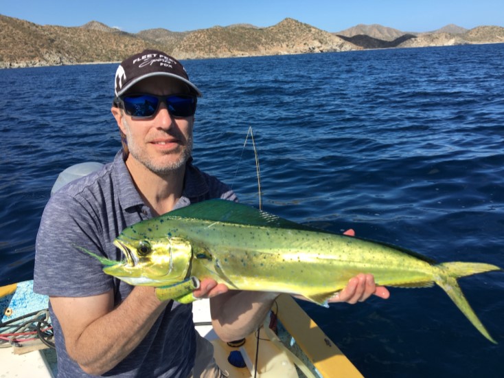 A man wearing a baseball cap and sunglasses holds up a sportfish