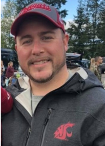 A man wearing a Washington Cougars hat and sweatshirt smiles for the camera