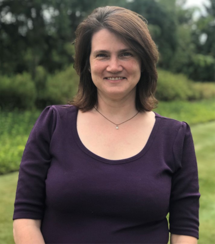 A woman in a purple shirt poses outdoors, smiling for the camera