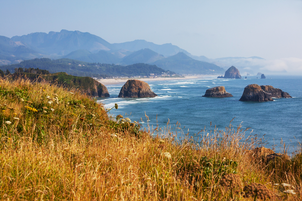 A coastal scene with blue water, large rocks, and coastal mountains.