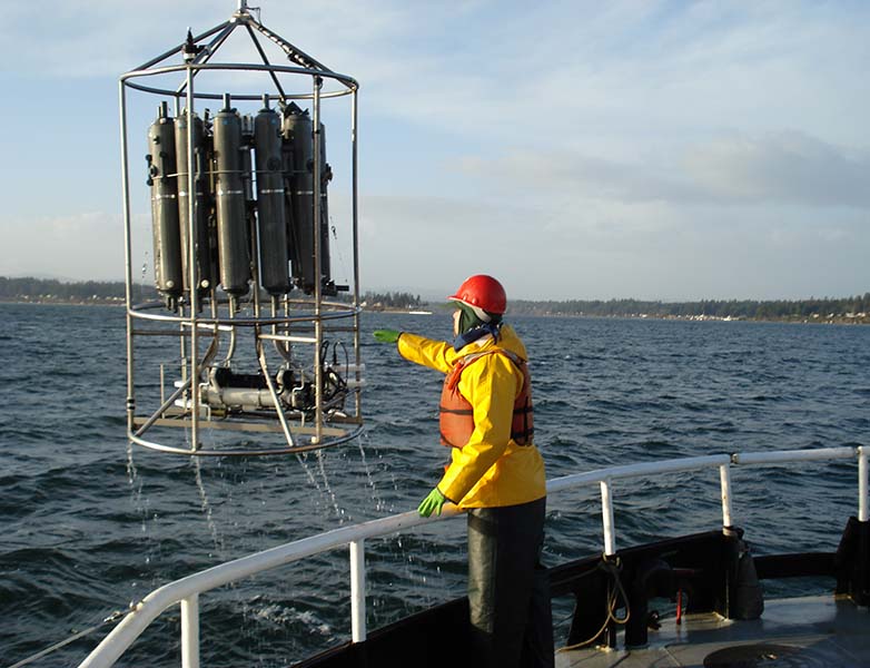 A scientist reaches out to a large array of sensors hanging off a boat.