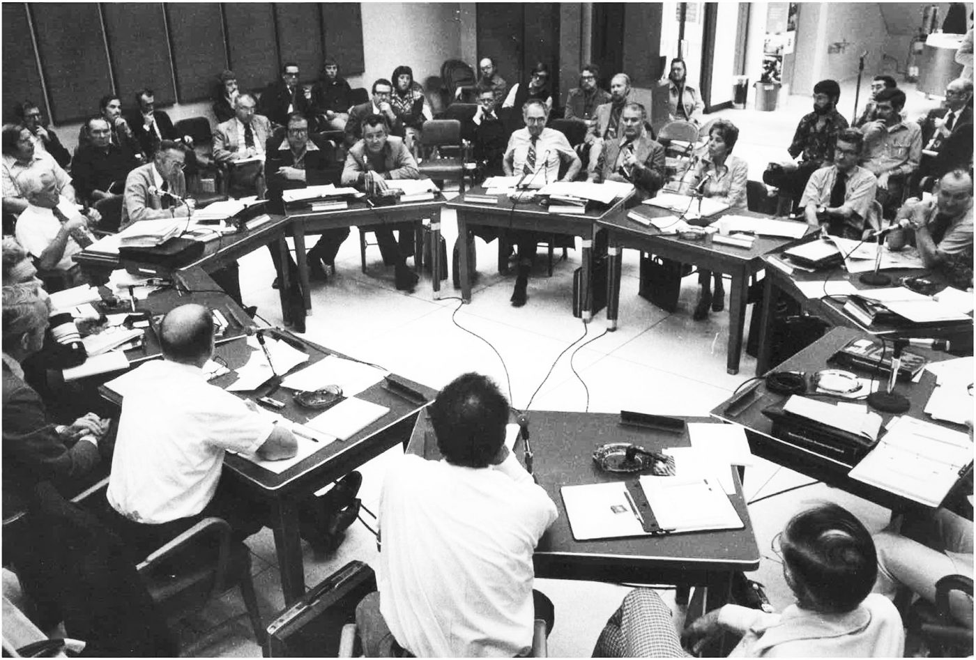 About 20 men and one woman sit around a table in the 1970s